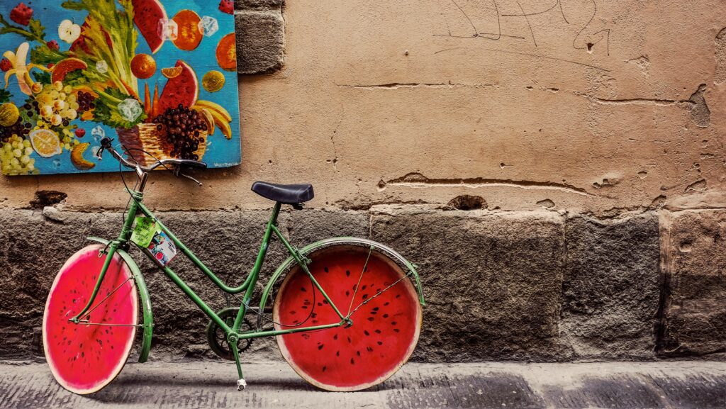 Green bicycle with watermelon-designed wheels leaning against a wall with a colorful fruit painting | Italian Digital Nomad Visa
